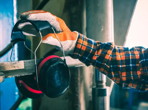 A worker reaches for the ear defenders in order protect himself from a loud machine.