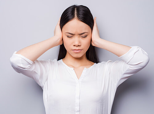 Without sound insulation, noise becomes an irritation. A young lady holds her ears in order to avoid the noise.